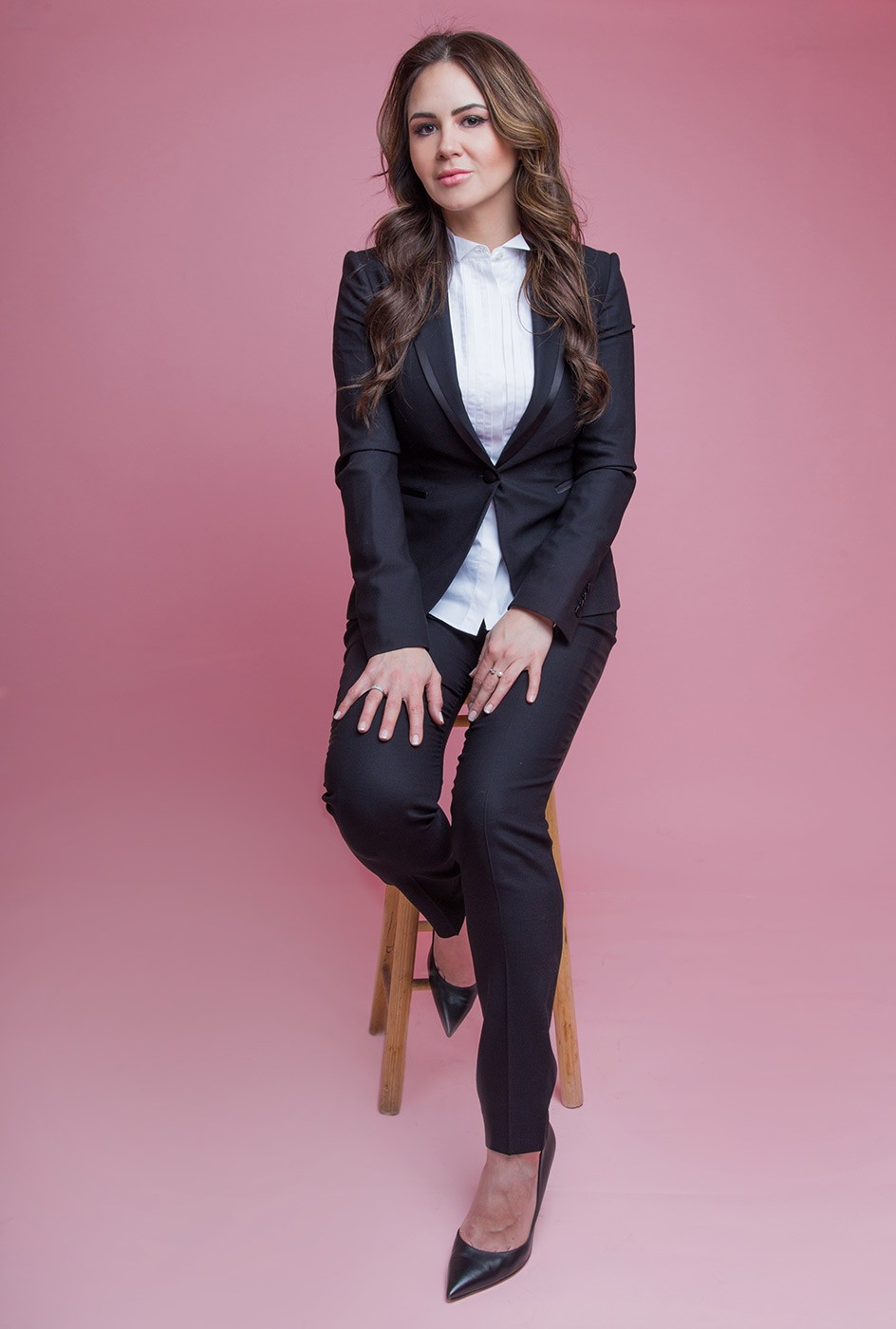 Viridiana sitting down on a chair in a pink background